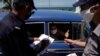 La policía revisa el lunes los documentos de los pasajeros de un auto en el punto de control de Boca de Jaruco, en Mayabeque, antes de remitirlos al personal sanitario que les tomará la temperatura (Alexandre Meneghini/Reuters).