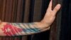 Un hombre con la bandera cubana tatuada en el brazo toca una de las barras de la cerca de la frontera de EEUU con México, en Ciudad Juarez. (Photo by HERIKA MARTINEZ/AFP/Archivo)